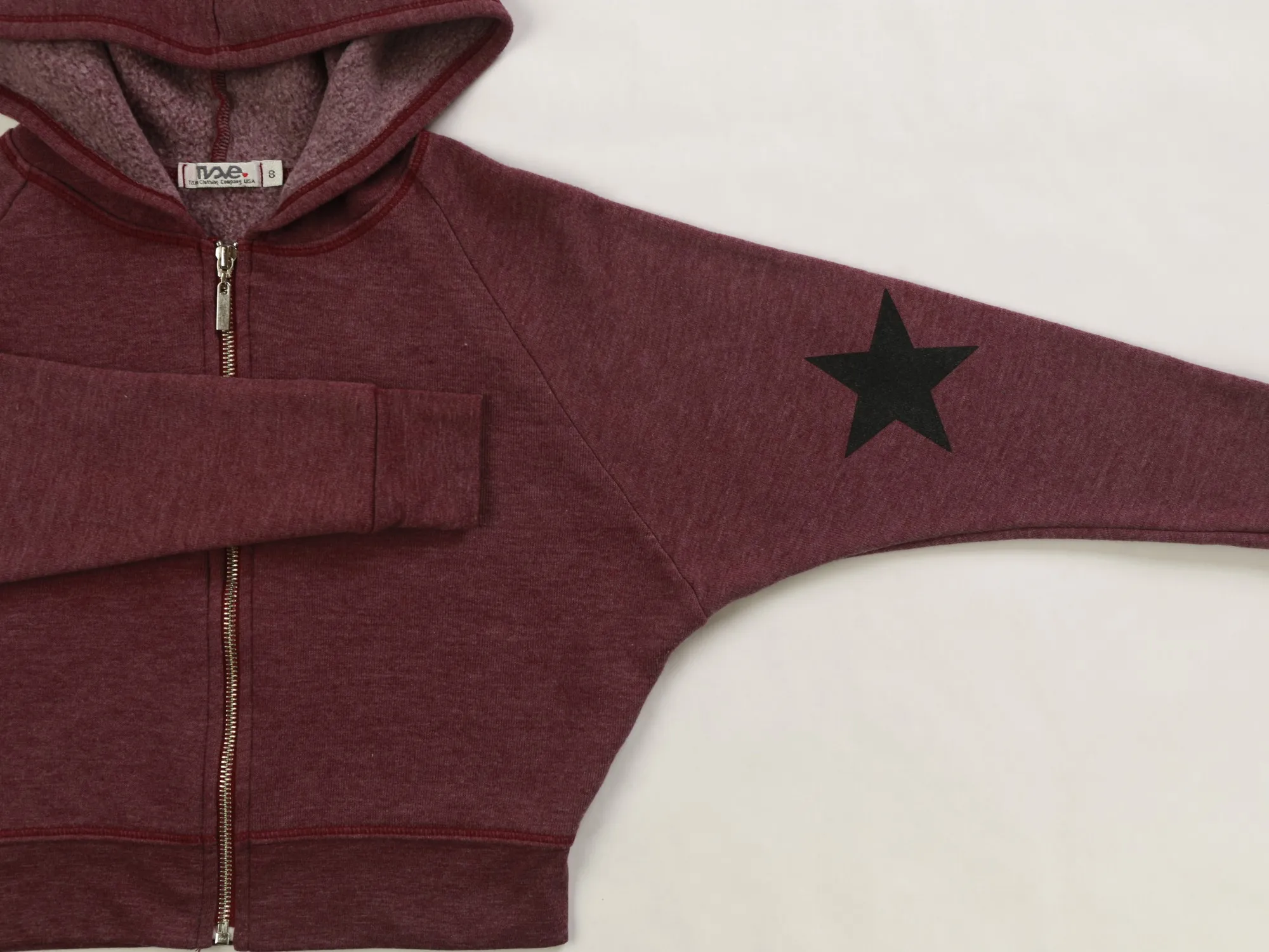 Close-up of the burgundy hoodie's sleeve star print, metal zipper, and woven size label