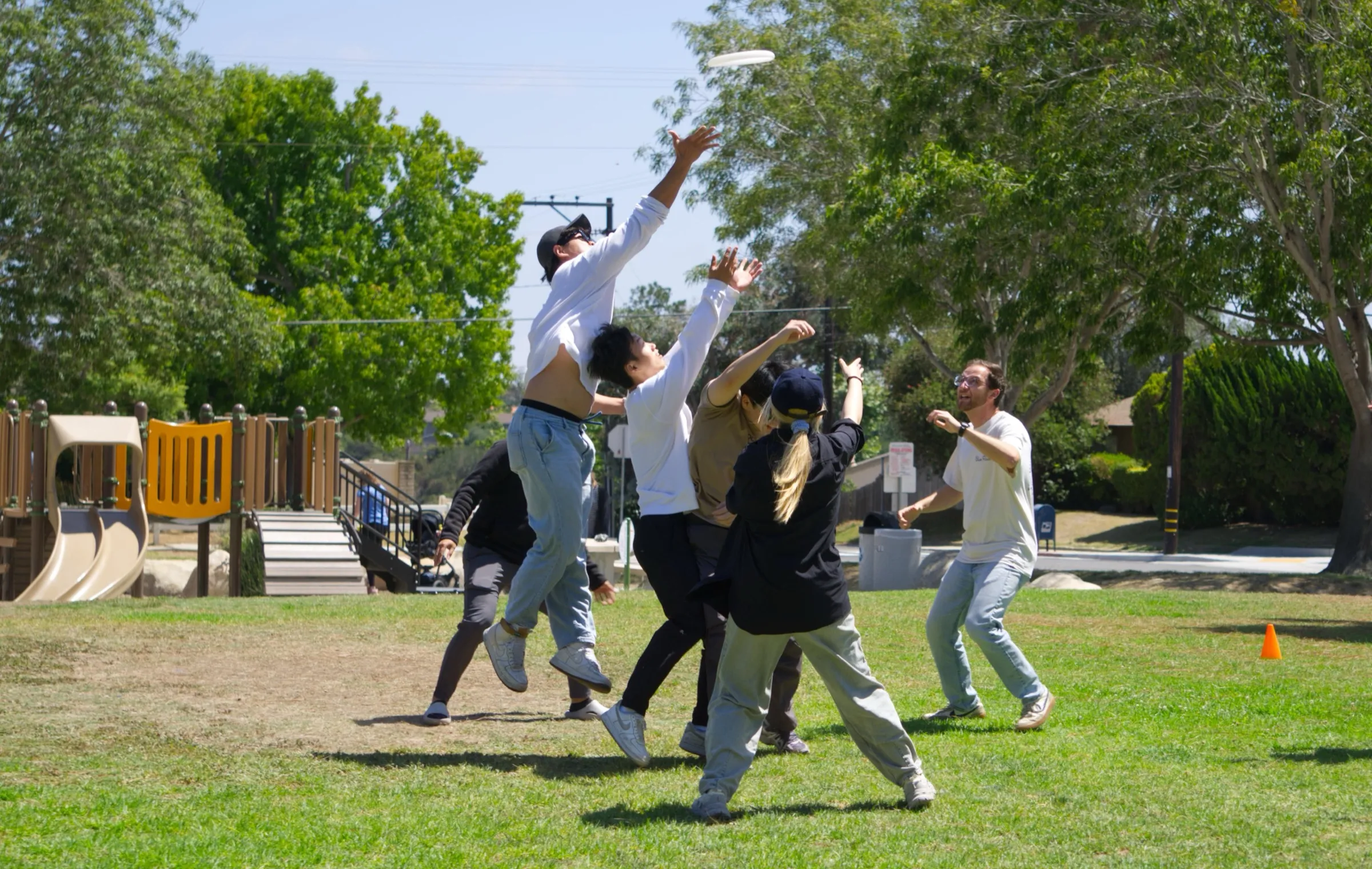 Players leaping for a frisbee mid-air at a sunny park pickup game