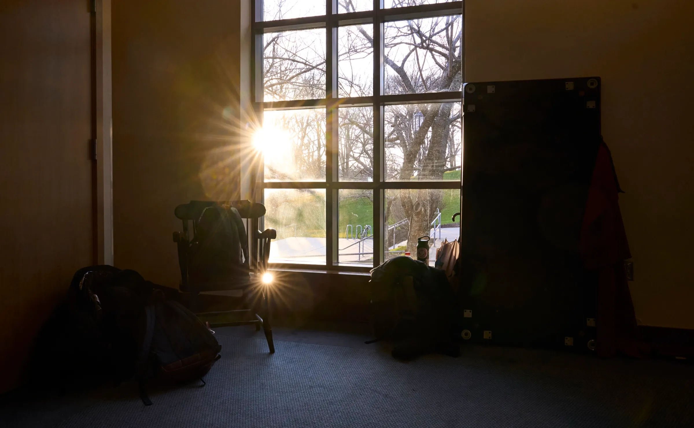 Sunburst through a paned window into a quiet room with a chair and backpacks