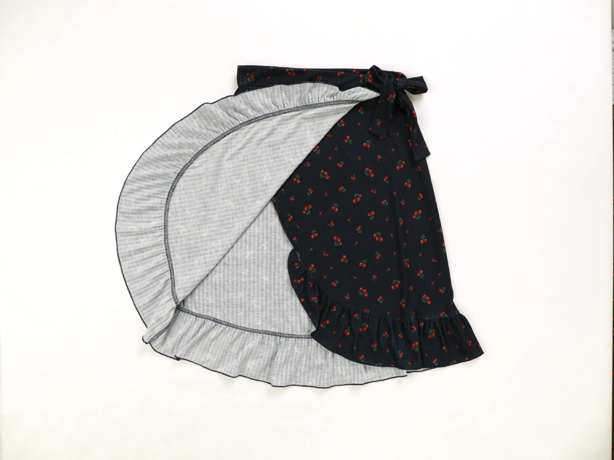 The cherry-print wrap skirt opened to show its striped grey lining and ruffle edge