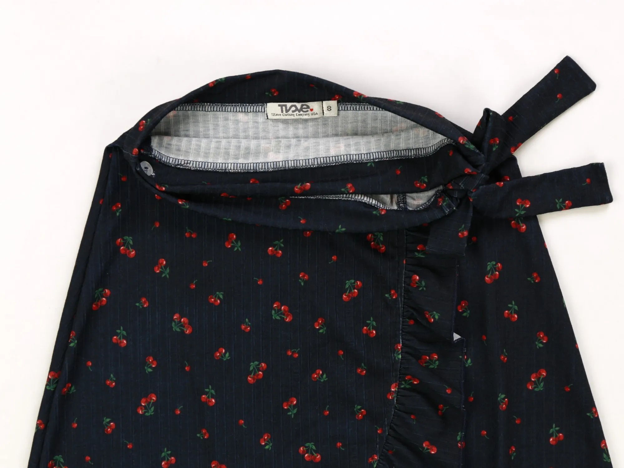 Close-up of the cherry-print skirt's waist tie, ruffle placket, and T2Love size label